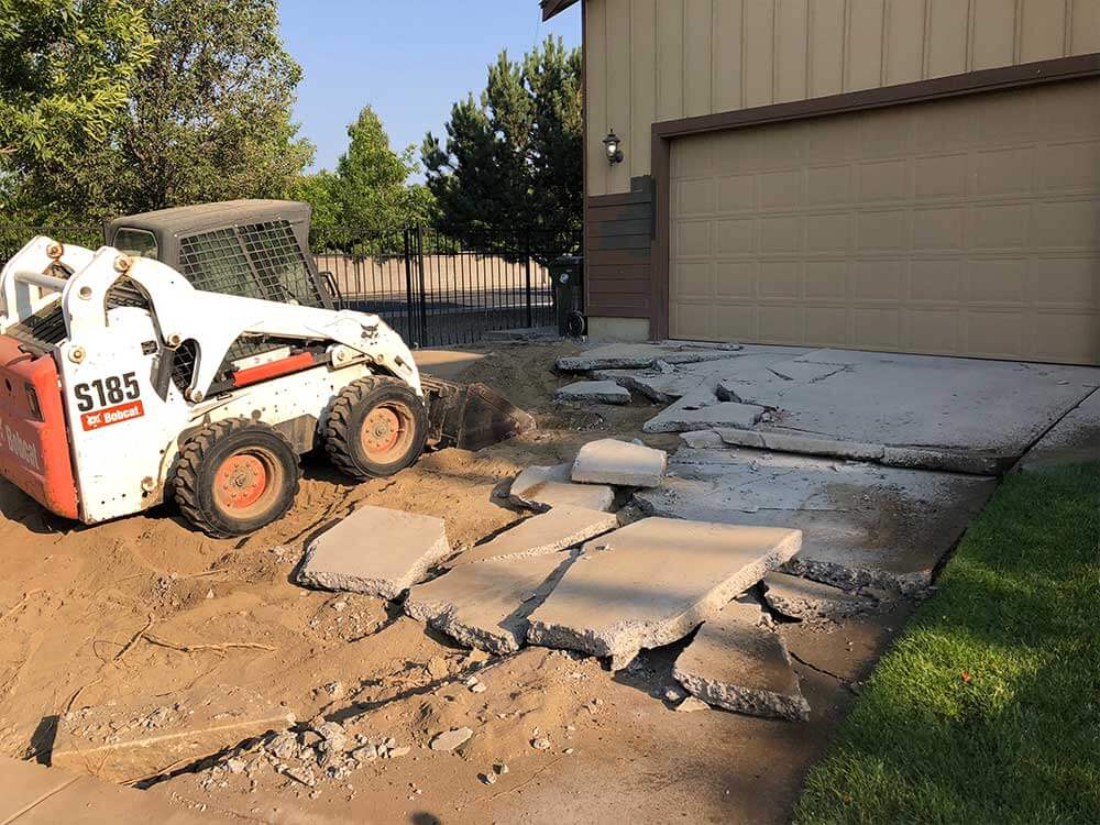 A skid steer removing concrete chunks out of a driveway 